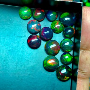 May include: A collection of 15 black opal cabochons in a variety of sizes and shapes. The opals are iridescent with shades of green, blue, red, and orange.