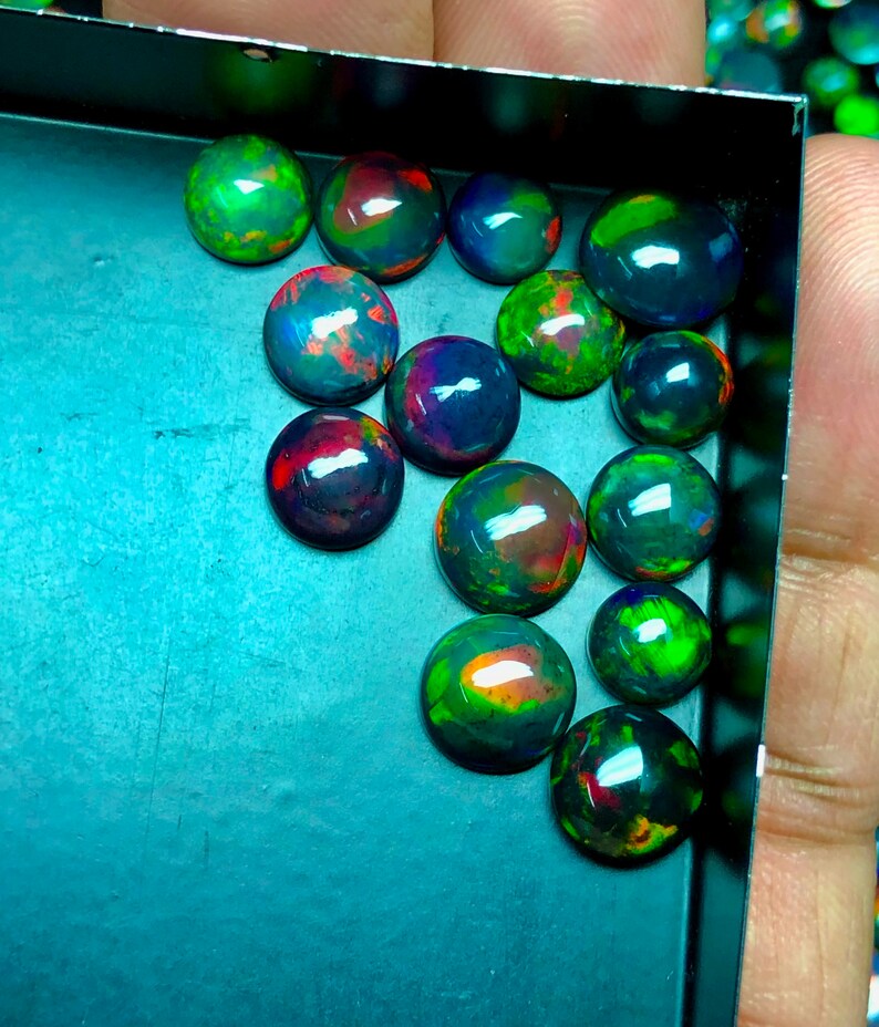May include: A collection of 15 black opal cabochons in a variety of sizes and shapes. The opals are iridescent with shades of green, blue, red, and orange.