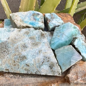 May include: A collection of blue and green ocean jasper rough stones. The stones are various sizes and shapes, with a swirling pattern of blue, green, and white.