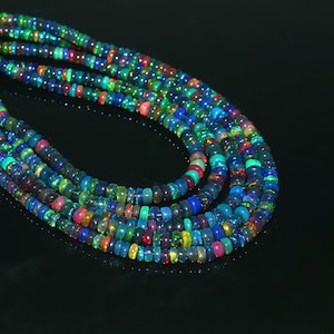 May include: Strands of colorful opal beads in a variety of colors including blue, green, red, and yellow. The beads are round and strung together, creating a layered effect. The opals have a dark base color.