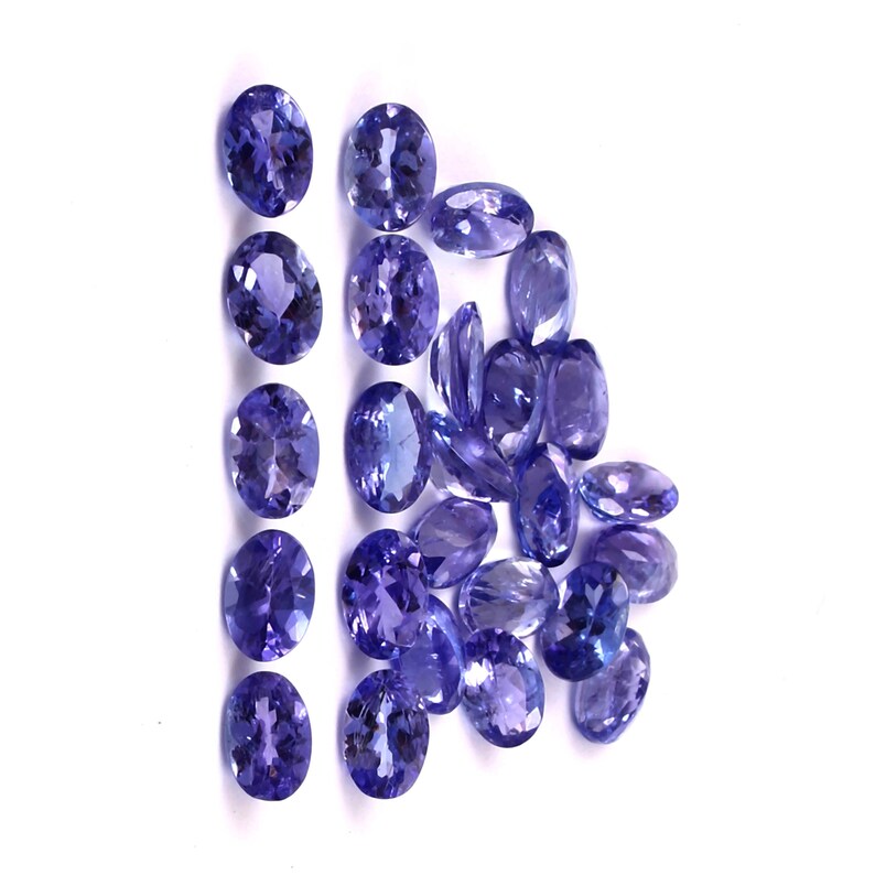 Puede incluir: Una colecci&oacute;n de piedras preciosas ovaladas de color p&uacute;rpura. Las piedras preciosas est&aacute;n dispuestas en una l&iacute;nea y un racimo.