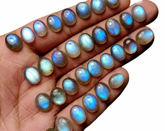 Peut inclure: Une collection de pierres précieuses de labradorite de forme ovale, avec une gamme de teintes irisées bleues et vertes. Les pierres sont disposées en rangées sur une main, mettant en valeur leur éclat et leur scintillement uniques.