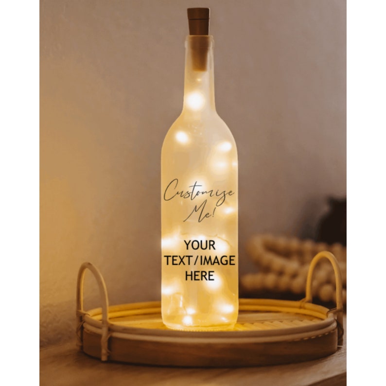 May include: A clear glass bottle with a cork top and a string of white lights inside. The bottle has the text "Customize Me!" and "YOUR TEXT/IMAGE HERE" printed on it. The bottle is sitting on a woven tray.