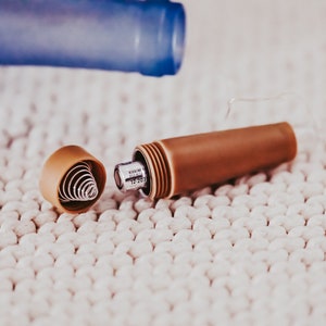 May include: A brown and silver metal pen with a spring mechanism inside the cap. The pen is open and the spring is visible. The pen is on a white surface.