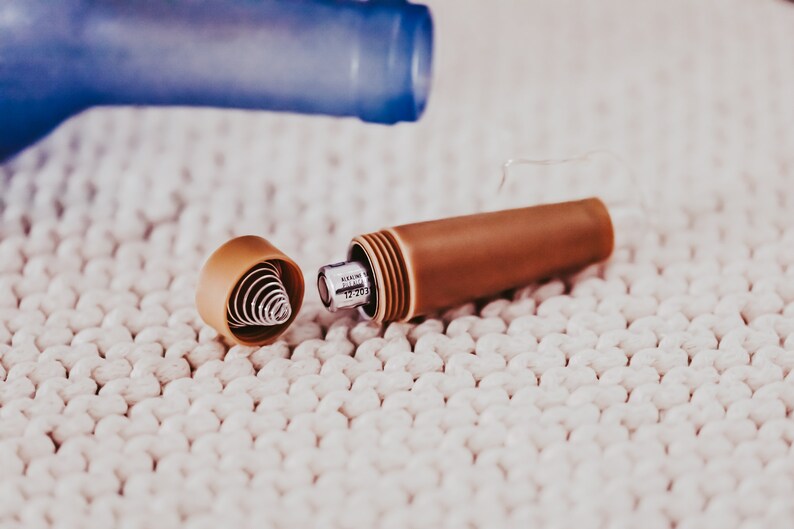 May include: A brown and silver metal pen with a spring mechanism inside the cap. The pen is open and the spring is visible. The pen is on a white surface.