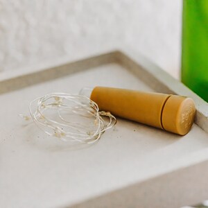 May include: A set of white fairy lights wrapped around a cork bottle stopper. The stopper is a light brown color and is made of cork.