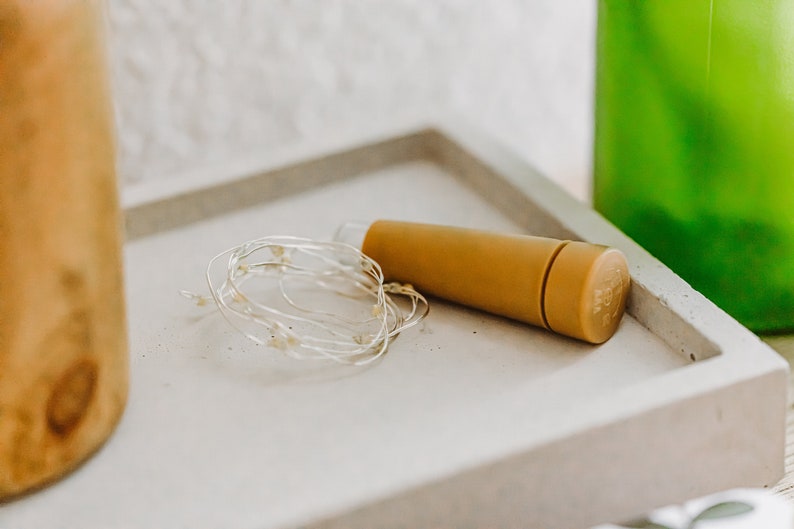 May include: A set of white fairy lights wrapped around a cork bottle stopper. The stopper is a light brown color and is made of cork.