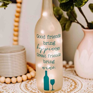 May include: A frosted glass wine bottle with a teal and white design. The bottle has a quote that reads "Good friends bring happiness. Great friends bring wine."