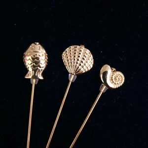May include: Three gold-toned metal pins with different sea-life designs. The pins feature a fish, a seashell, and a snail.