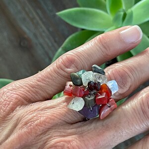 May include: A ring made of various colorful stones, including red, green, purple, and white. The stones are clustered together in a random pattern, creating a unique and eye-catching design.