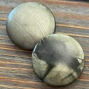 May include: Two round, wooden cabinet knobs with a light, natural finish. The knobs have a slightly domed shape and visible wood grain. One knob has a darker, more distressed appearance. The knobs are likely for furniture or decorative use.