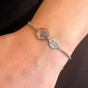 May include: A silver bracelet with a hexagonal charm containing a pressed flower and a round charm with the inscription "My Mum My Rock".