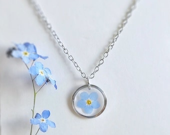 May include: A silver necklace with a delicate pendant featuring a pressed forget-me-not flower in a clear resin circle.