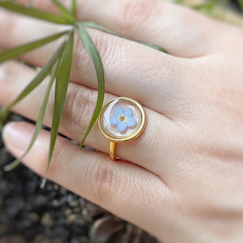 May include: A gold ring with a clear round bezel containing a pressed forget-me-not flower.