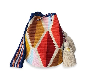 May include: A bucket bag featuring a geometric diamond pattern in shades of red, orange, yellow, brown, pink, and light blue. The bag has a dark blue drawstring top, a matching woven shoulder strap, and two large beige tassels with a gold charm.