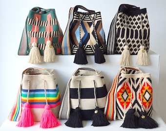 May include: Six bucket bags with woven patterns and shoulder straps. The bags feature various designs including geometric shapes, stripes, and rainbow colors, each with drawstring closures, long tassels, and small gold-toned circular metal charms.