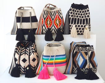 May include: Six bucket bags with woven patterns and shoulder straps. The bags feature various designs including black and white stripes, geometric shapes in red, yellow, and black, and a rainbow-colored bag. Each bag has drawstring closures with tassels.