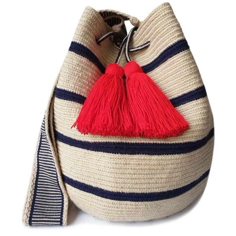 May include: A beige bucket bag featuring horizontal navy blue stripes, a drawstring closure, and two prominent bright red yarn tassels. The bag includes a wide, flat shoulder strap with a matching navy blue and beige striped pattern.