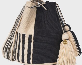 May include: A bucket bag crafted from woven fabric featuring a black and cream color scheme. The design includes vertical stripes on one side and a solid black panel on the other. It has a drawstring closure, a wide shoulder strap, and two large cream-colored tassels with a small gold-toned circular charm engraved with the text LOMENA.