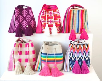 May include: Six bucket bags with shoulder straps and drawstring closures featuring various patterns and colors including magenta, pink, orange, blue, and beige. Each bag is adorned with two large hanging tassels at the front drawstring ends.