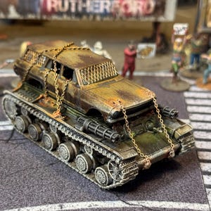 Puede incluir: Un modelo de veh&iacute;culo postapocal&iacute;ptico que presenta una carrocer&iacute;a de coche oxidada y desgastada, asegurada con finas cadenas met&aacute;licas sobre un chasis de tanque militar. Incluye ca&ntilde;ones laterales y malla protectora en las ventanas.