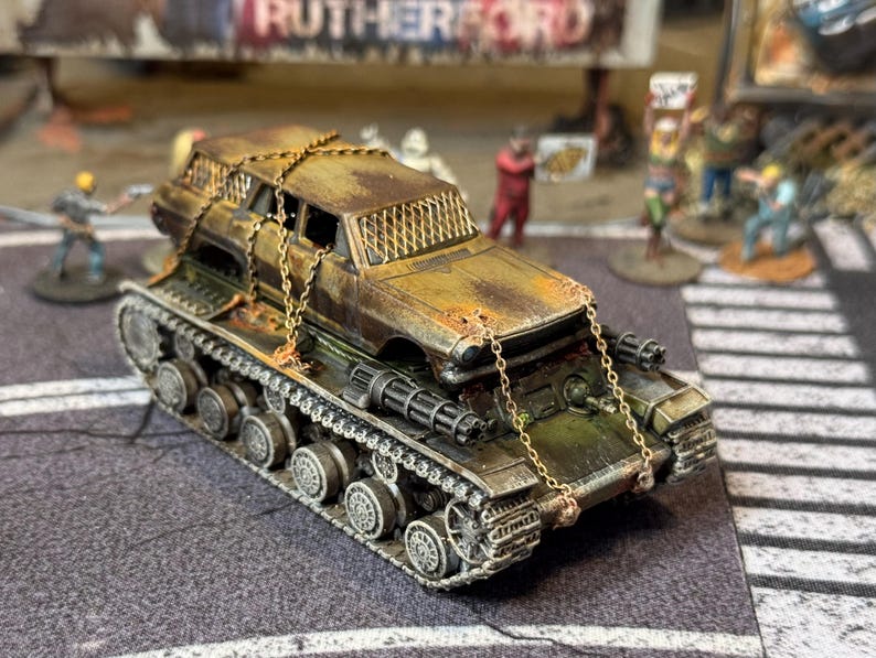 Puede incluir: Un modelo de veh&iacute;culo postapocal&iacute;ptico que presenta una carrocer&iacute;a de coche oxidada y desgastada, asegurada con finas cadenas met&aacute;licas sobre un chasis de tanque militar. Incluye ca&ntilde;ones laterales y malla protectora en las ventanas.