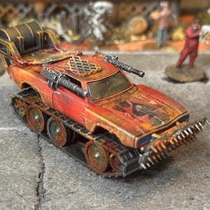 Puede incluir: Un veh&iacute;culo en miniatura postapocal&iacute;ptico con pintura desgastada en rojo y naranja, orugas de tanque, parachoques delantero con p&uacute;as, dos ca&ntilde;ones laterales, una rejilla en el techo y un gran tambor de carga trasero, con detalles de &oacute;xido.