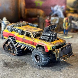 Puede incluir: Un veh&iacute;culo en miniatura postapocal&iacute;ptico pintado en amarillo y rojo con un acabado desgastado. Cuenta con una gran toma de aire en el cap&oacute;, un parachoques delantero con p&uacute;as, pinchos laterales, una ametralladora en el techo y orugas traseras.