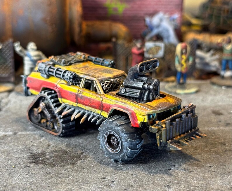 Puede incluir: Un veh&iacute;culo en miniatura postapocal&iacute;ptico pintado en amarillo y rojo con un acabado desgastado. Cuenta con una gran toma de aire en el cap&oacute;, un parachoques delantero con p&uacute;as, pinchos laterales, una ametralladora en el techo y orugas traseras.