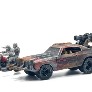 以下が含まれることがあります： 黒い炎のデカールが施された風化した赤いマッスルカー、屋根に取り付けられたガトリングガン、フロントのスパイク付きラムを備えたミニチュアの終末世界風のシーン。2体のグレーのフィギュアを乗せた小さなオートバイが付属しています。