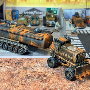 May include: A miniature, post-apocalyptic diorama featuring two weathered vehicles. One is a tracked tank with a cylindrical body and a gun turret. The other is a truck with a plow, both painted in shades of brown and orange, suggesting rust and decay.