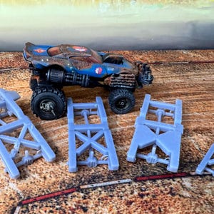 Könnte beinhalten: Ein blau-braunes Spielzeug-Monstertruck mit großen schwarzen Reifen und vier hellblauen Kunststoff-Rahmenteilen. Der Truck hat ein verwittertes Aussehen, was auf ein postapokalyptisches Thema hindeutet. Die Teile sind nicht montiert.