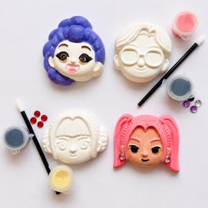 Pode incluir: Um kit de artesanato com quatro rostos de personagens esculpidos, dois pinc&eacute;is pretos, quatro pequenos potes de tinta nas cores rosa, preta, amarela e branca, e v&aacute;rios pequenos strass adesivos nas cores vermelha, roxa e transparente.