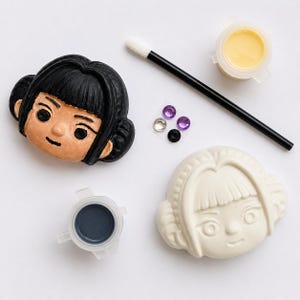 Pode incluir: Um kit de artesanato com duas cabe&ccedil;as de personagem esculpidas, uma pintada de preto e outra branca sem pintura. Inclui um pincel aplicador preto, um pequeno recipiente de tinta amarela, um de tinta cinza-escura e quatro gemas adesivas.