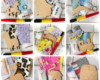 May include: A collection of craft kits featuring wooden cutouts of various shapes, including a unicorn, dolphin, llama, train, dinosaur, flamingo, and a van. Each kit includes fabric scraps, a keychain ring, and a marker. The kits are arranged on a white brick background.
