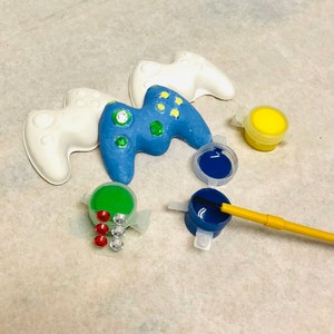 Peut inclure: Une manette de jeu en céramique peinte en bleu et vert avec des manettes de jeu en céramique blanches, des pots de peinture et des strass.