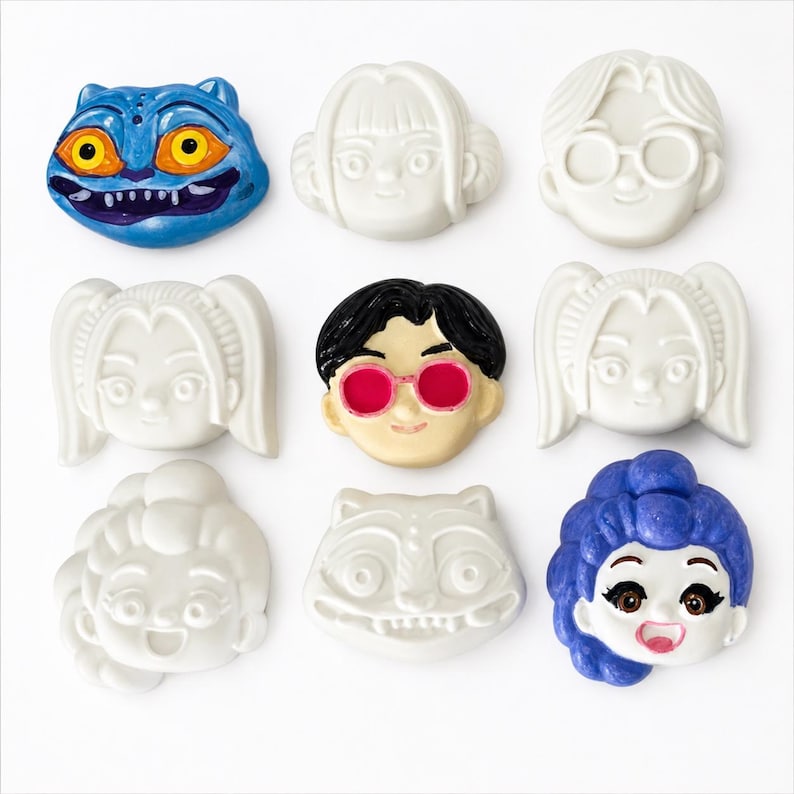 Pode incluir: Uma cole&ccedil;&atilde;o de nove broches ou pingentes em forma de cabe&ccedil;a esculpida. O conjunto inclui v&aacute;rios personagens com caracter&iacute;sticas distintas, alguns em branco s&oacute;lido e outros com detalhes pintados como pelo azul, &oacute;culos rosa, cabelo preto e cabelo roxo.
