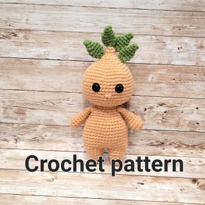 Pode incluir: Padrão de crochê para uma boneca de crochê bege fofa com um topo de folhas verdes. A boneca tem olhos pretos e um sorriso simples.