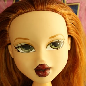 Könnte beinhalten: Ein Bratz-Puppenkopf mit rotbraunem Haar, grünen Augen und dunkelroten Lippen. Die Puppe ist auf einem sternförmigen Sockel montiert. Der Hintergrund ist dunkelblau mit rosa Text.