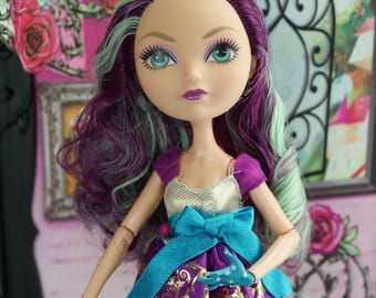 May include: A fashion doll with purple and green hair, dressed in a purple dress with a blue bow and gold detailing. The doll wears blue gloves and white shoes. The background features a decorative mirror and floral wallpaper.