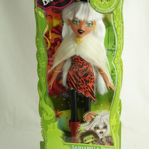 Könnte beinhalten: Eine SashaBella Paws-Puppe von Bratzillaz in einer grünen Verpackung. Die Puppe hat weißes Haar, grüne Augen und ein rot-schwarz gemustertes Kleid. Die Verpackung trägt die Aufschrift "Bratzillaz" und "SashaBella Paws".