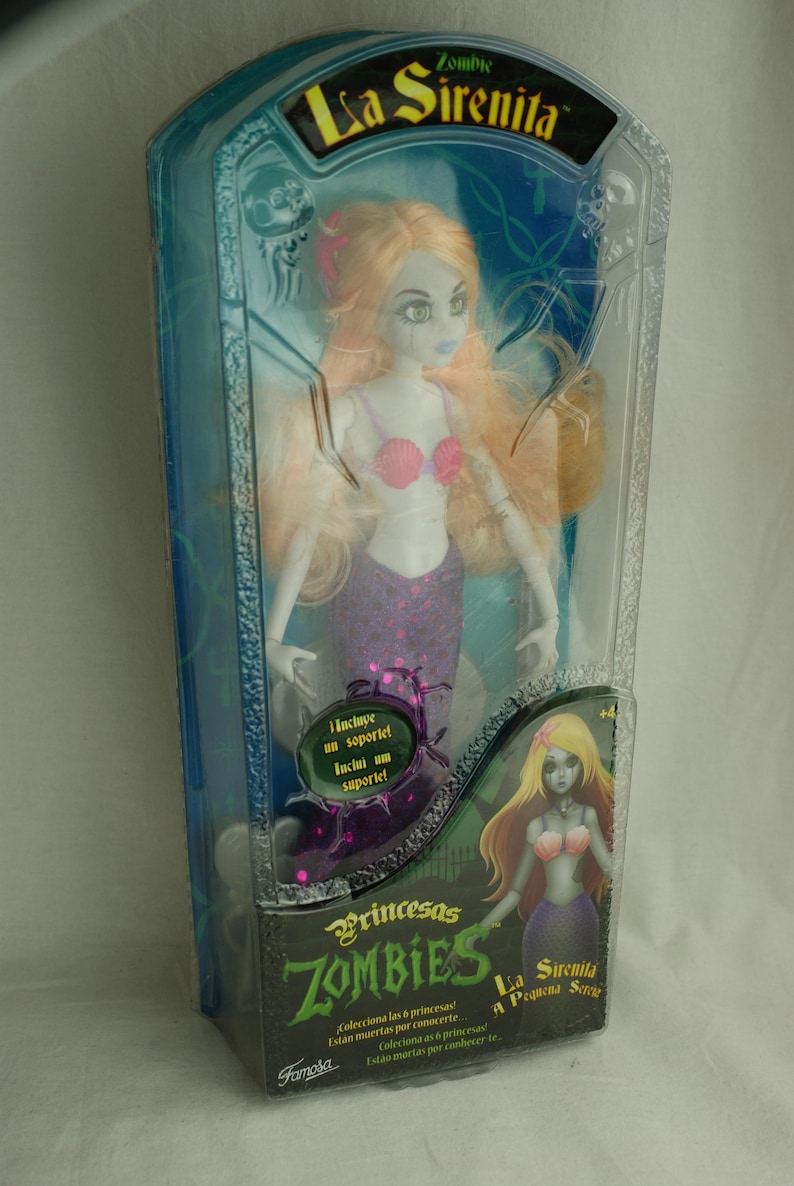 May include: A Zombie La Sirenita doll in original packaging. The doll has pale skin, long light orange hair, a pink seashell top, and a purple tail. The box features the text Zombie La Sirenita, Princesas ZOMBIES, and La Sirenita A Pequena Sereia.
