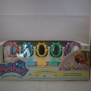 Puede incluir: Un juego de juguetes Bidibodi en caja, con cinco espejos de juguete coloridos en rosa, azul, amarillo, verde y morado. El embalaje incluye el texto "Bidibodi" y "Divertiti 5 volte di più!" con una ilustración de una niña.