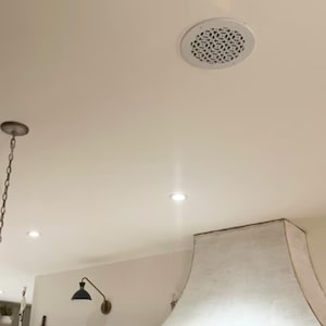 May include: White ceiling with recessed lighting and a round ceiling vent with a decorative pattern. A white kitchen range hood with a fabric canopy is visible in the bottom right corner of the image.
