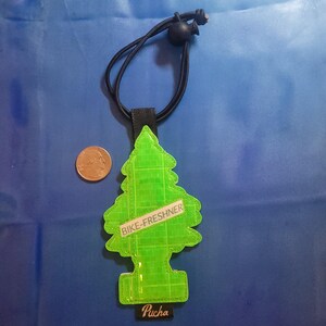 May include: A neon green, tree-shaped air freshener with the text "BIKE-FRESHNER" and "Pucha". It has a black elastic cord and a black fabric loop. A U.S. quarter is next to the air freshener.