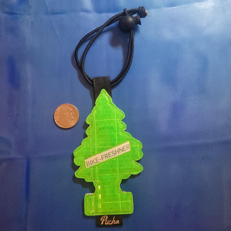 May include: A neon green, tree-shaped air freshener with the text "BIKE-FRESHNER" and "Pucha". It has a black elastic cord and a black fabric loop. A U.S. quarter is next to the air freshener.