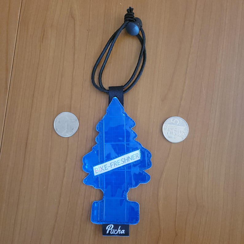 May include: A blue, pine-tree-shaped air freshener with the text "BIKE-FRESHNER" and "Pucha". It has a black cord for hanging. Two coins are on either side of the air freshener.