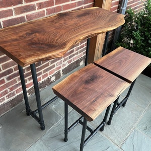 May include: A set of three wooden bar stools with black metal legs. The stools are made from walnut wood and have a live edge design. The stools are arranged in a row on a gray tiled floor.