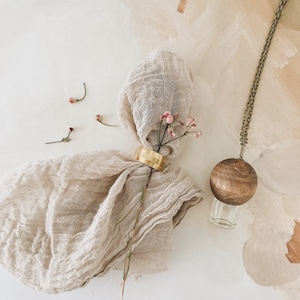 May include: A wooden diffuser pendant with a gold ring and a sprig of dried pink flowers on a beige fabric background.
