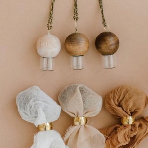 May include: Three wooden diffuser pendants with glass bottles and fabric tassels in beige, white, and brown.